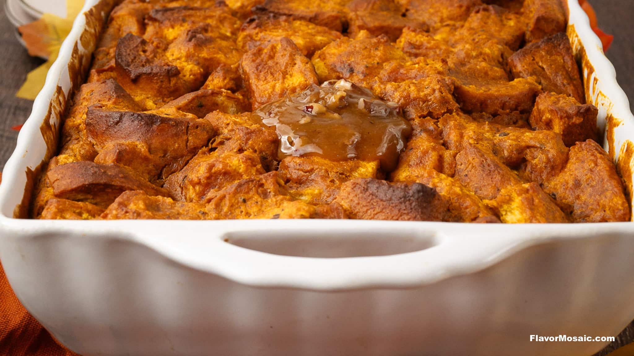 A white baking dish filled with golden brown Pumpkin Praline Bread Pudding, topped with a dollop of melting butter or sauce in the center.