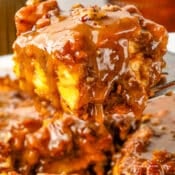 A gooey slice of Pumpkin Praline Bread Pudding covered in caramel sauce is lifted from a dish, showing its moist texture and pecan topping.