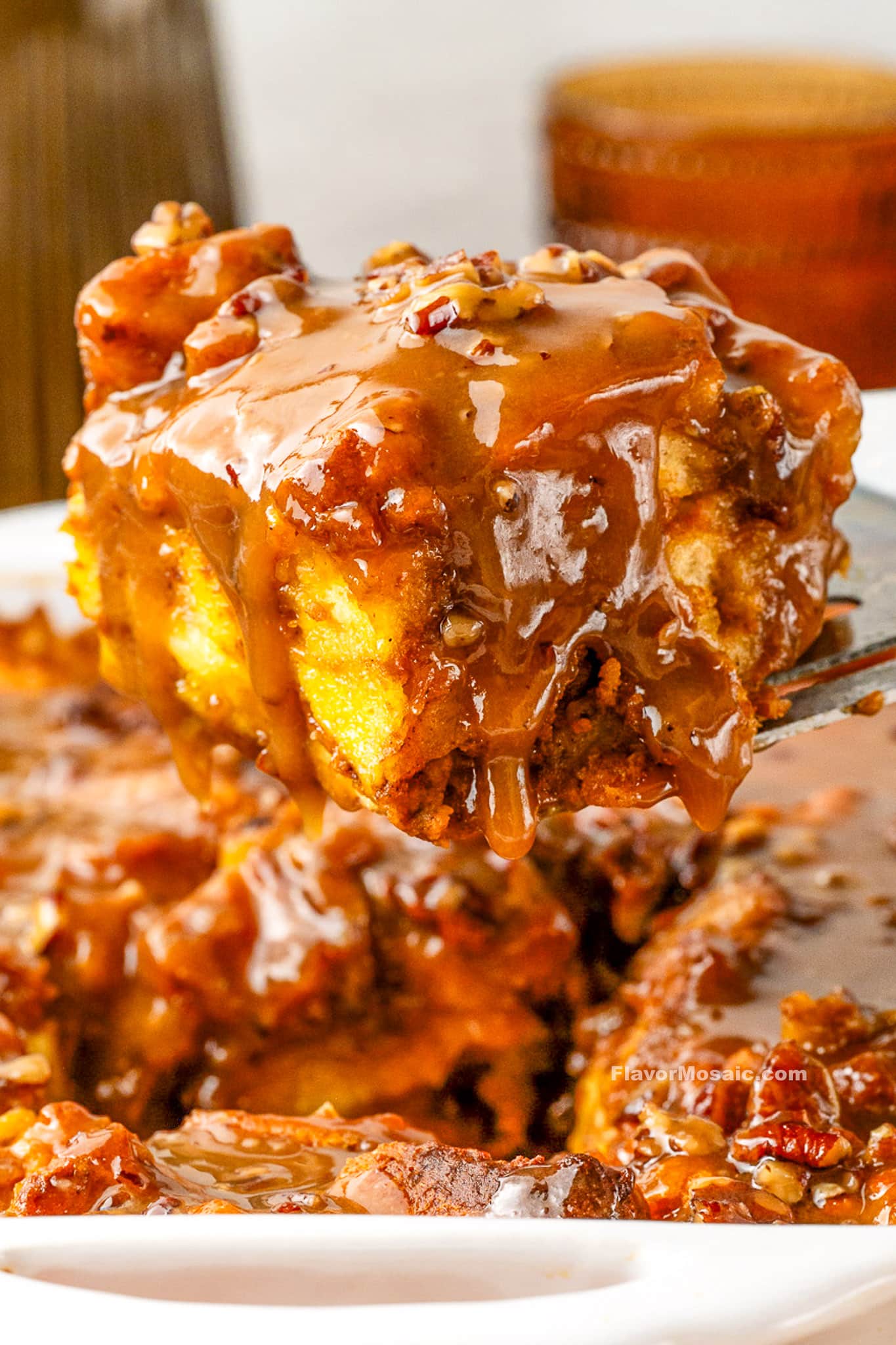 A gooey slice of Pumpkin Praline Bread Pudding covered in caramel sauce is lifted from a dish, showing its moist texture and pecan topping.