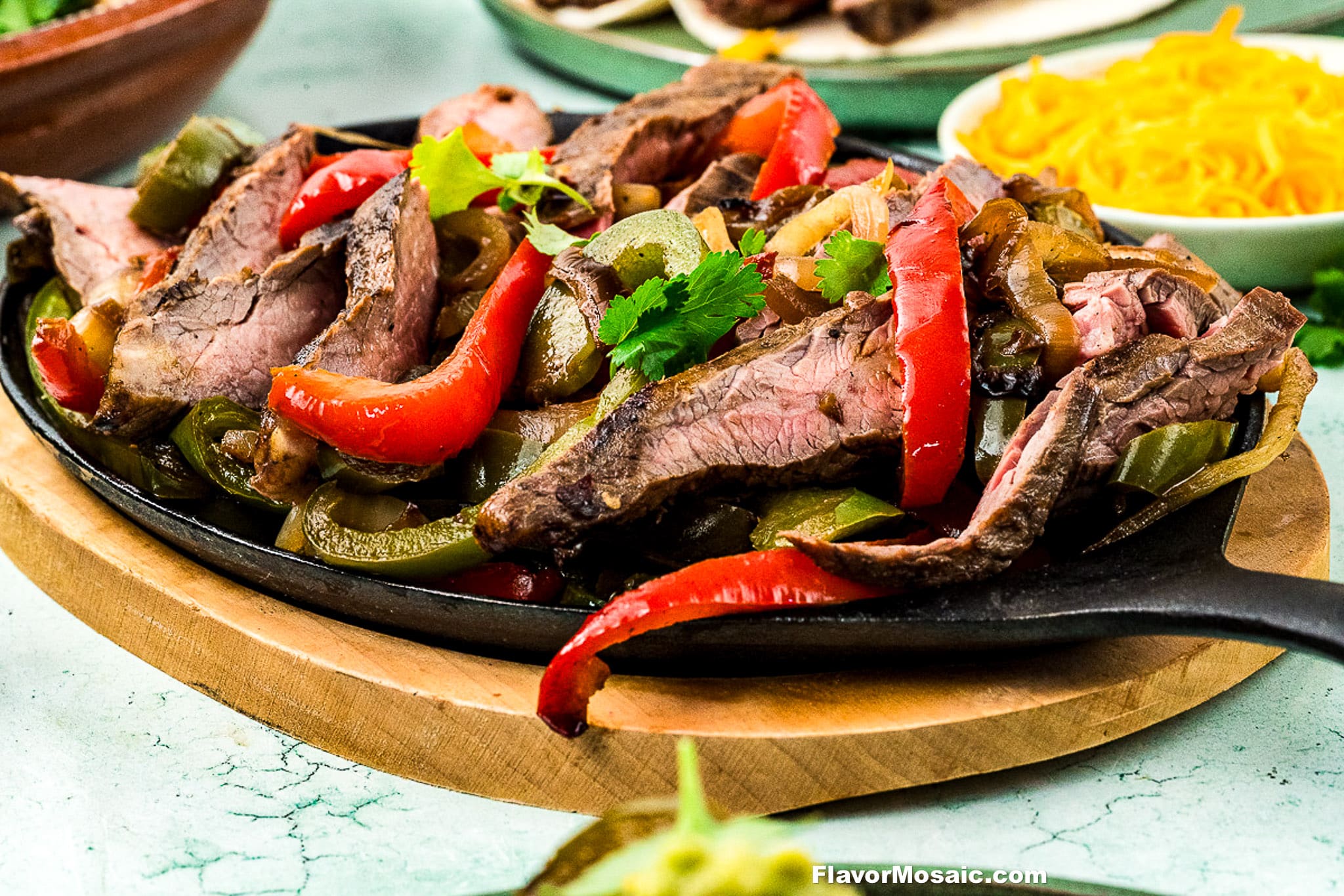 Sizzling Tex-Mex Beef Fajitas with grilled steak slices, red and green bell peppers, and onions served on a cast iron skillet, garnished with cilantro. A bowl of shredded cheese is visible in the background.