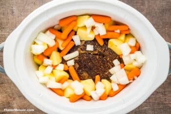A white Crock Pot contains a chuck roast in the center, surrounded by neatly arranged, uncooked potatoes, carrots, and onions—perfect for making a classic Crock Pot Chuck Roast.