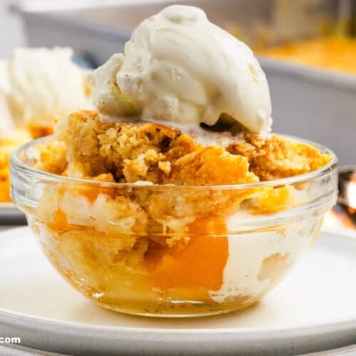 Side view of single serving of peach cobbler dump cake in a small clear bowl.