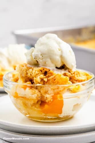 Side view of a single serving of peach cobbler dump cake served in a small clear bowl and topped with a scoop of ice cream.
