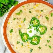 Overhead photo of red bowl on white plate with Instant Pot White Chicken Chili topped with sour cream, jalapeños, and cilantro