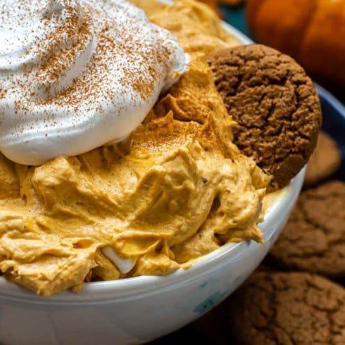 A bowl of Pumpkin Fluff with Cool Whip And Marshmallows and served on a plate with gingerbread snaps.