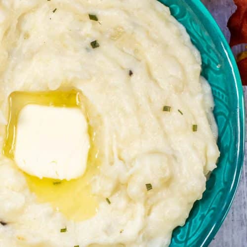 Overhead view of 2/3 of bowl of mashed potatoes with a pat of butter partially melted in an aqua bowl.