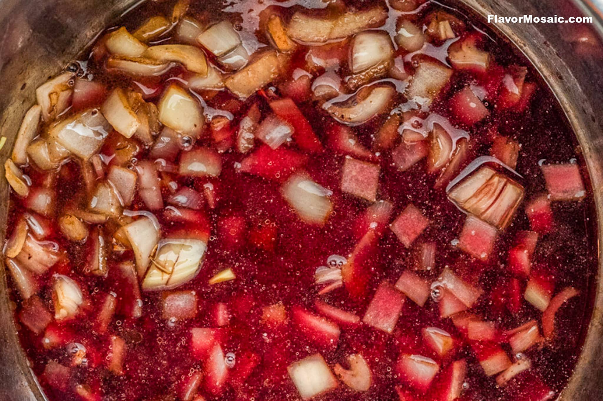 A close-up of a pot filled with red liquid, diced onions, and small chunks of vegetables, possibly in the process of making Beef Stew. The ingredients are partially submerged and floating on the surface.