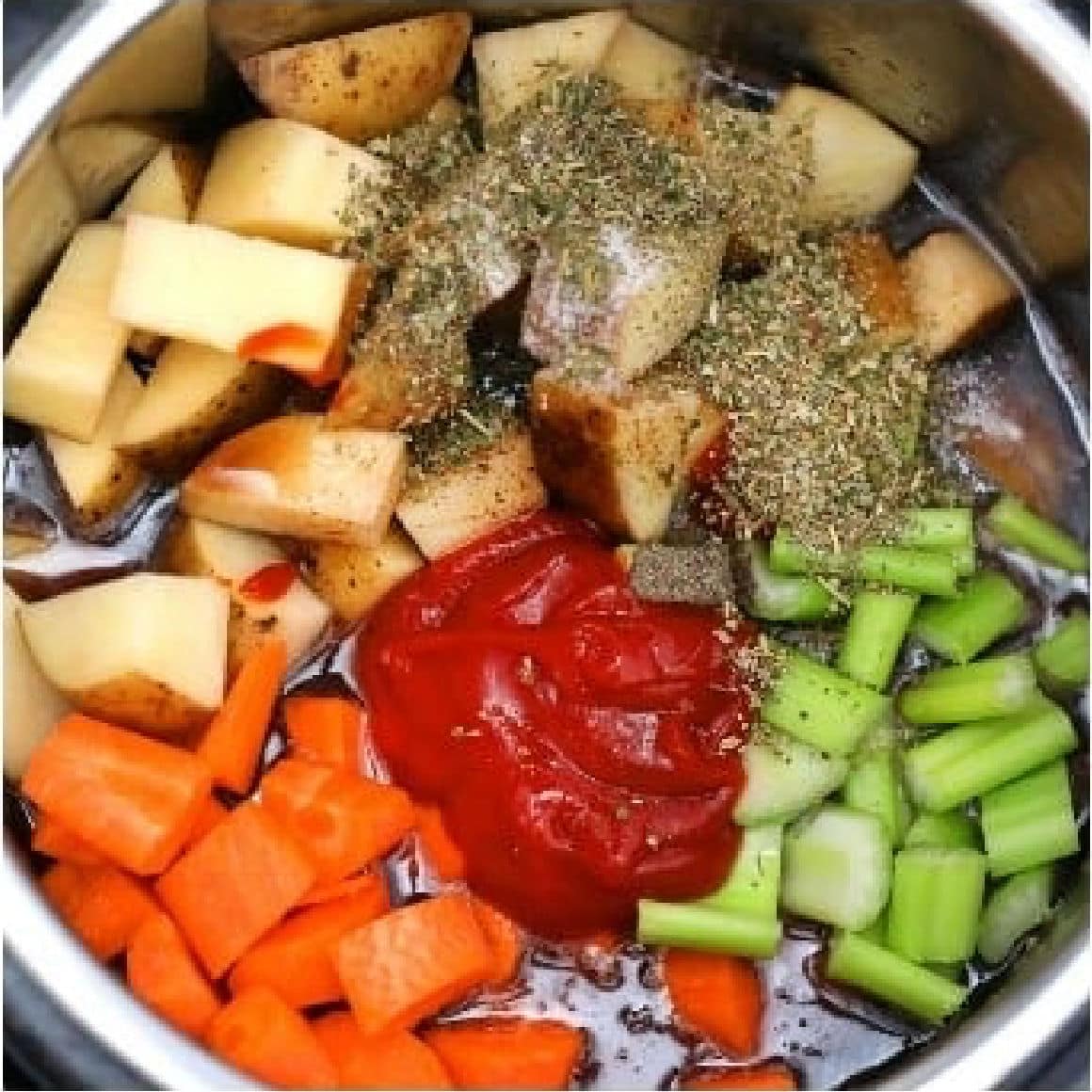 Chopped potatoes, celery, and carrots with ketchup, herbs, and seasoning in a metal pot-perfect ingredients for a hearty Beef Stew.