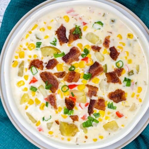 Overhead view of a white bowl of corn chowder topped with bacon and green onions sitting on a blue napkin.