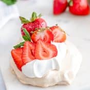 Strawberry Mini Pavlova sitting on white marble with fresh strawberries in the background.