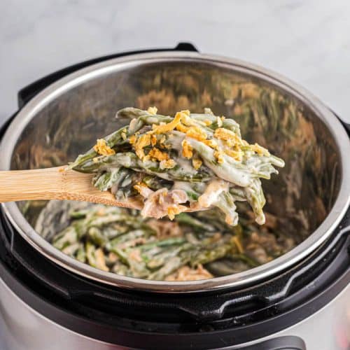 Holding spoonful of green bean casserole over Instant Pot with the rest of the green bean casserole