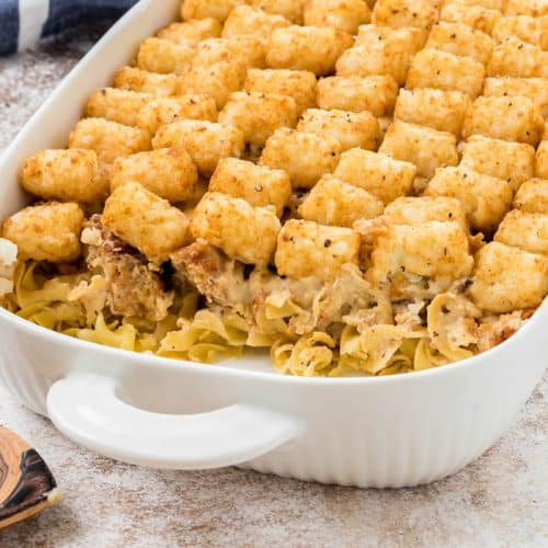 View of the whole dish, minus one scoop, of Chicken Bacon Tater Tot Casserole with blue napkin in the background.