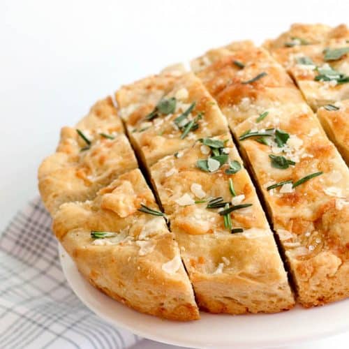 Golden Asiago Foccacia sitting on elevated white patter cut into slices.
