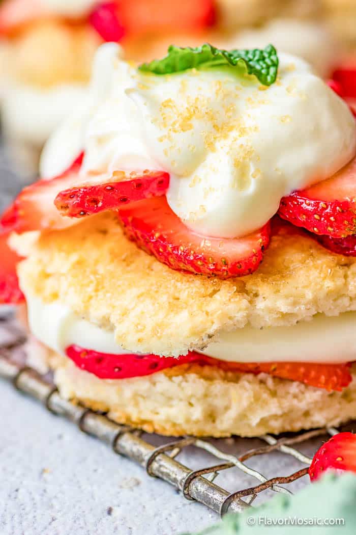 Close-up of a classic Strawberry Shortcake with fresh sliced strawberries, whipped cream, and a biscuit, garnished with a mint leaf, resting on a metal cooling rack.
