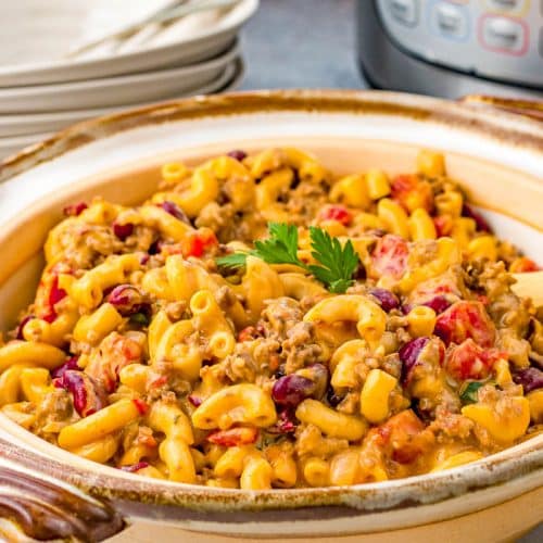 Bowl of Instant Pot Chili Mac with plates behind it and a partial view of the Instant Pot behind it.