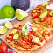 BBQ Chicken Tostadas on a cutting board surfing by tomatoes, limes, and avocado.