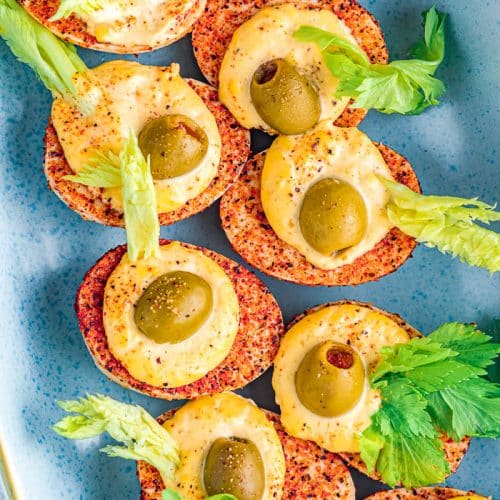 Overhead view of bloody mary deviled eggs with green olives and celery leaves.