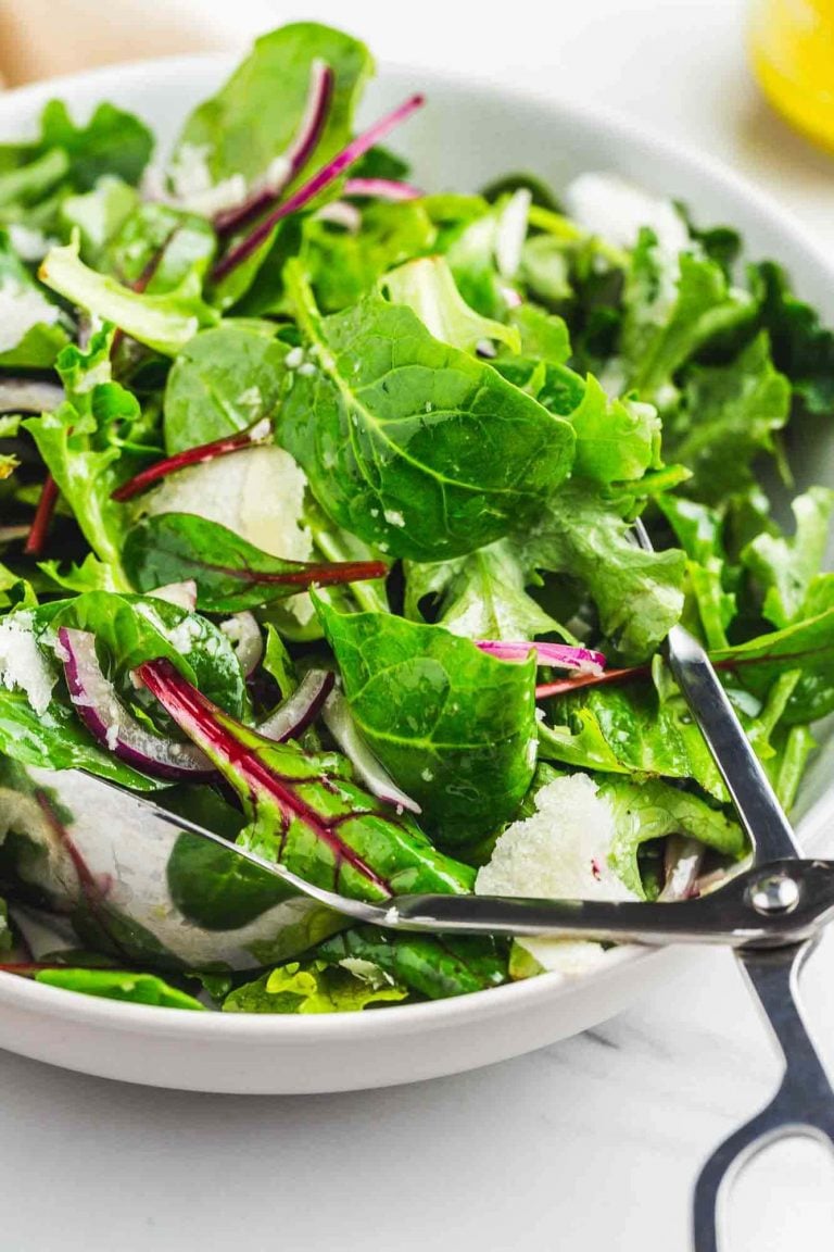 Simple tossed green salad in a white bowl with metal tongs