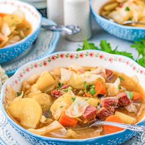 Bowl of Slow Cooker Corned Beef and Cabbage Soup in a blue bowl with partial views of 2 other soup bowls in the background.