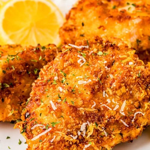 Air fryer parmesan chicken on a white plate with lemon and a peek of a red and white checkered napkin in back