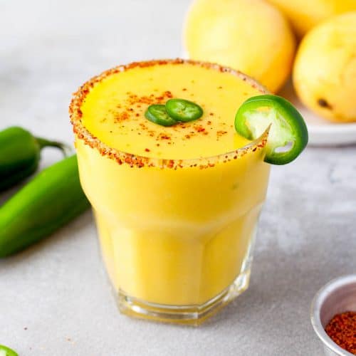 1 glass yellow mango jalapeño margarita with jalapeno slices and rimmed with tajin.