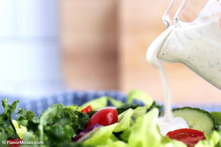 A close-up of creamy ranch dressing being poured onto a fresh green salad with lettuce, tomato, and cucumber slices.