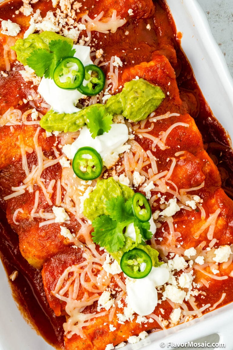 Overhead close up of Enchiladas Rancheras topped wtih cheese sour cream, avocados, jalapenos, and chopped cilantro.