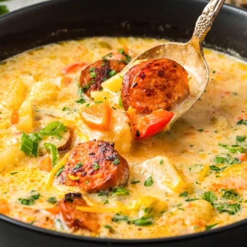 A spoonful of Slow Cooker Cajun Potato Soup held slightly above the rest of the bowl of potato soup with andouille sausage.