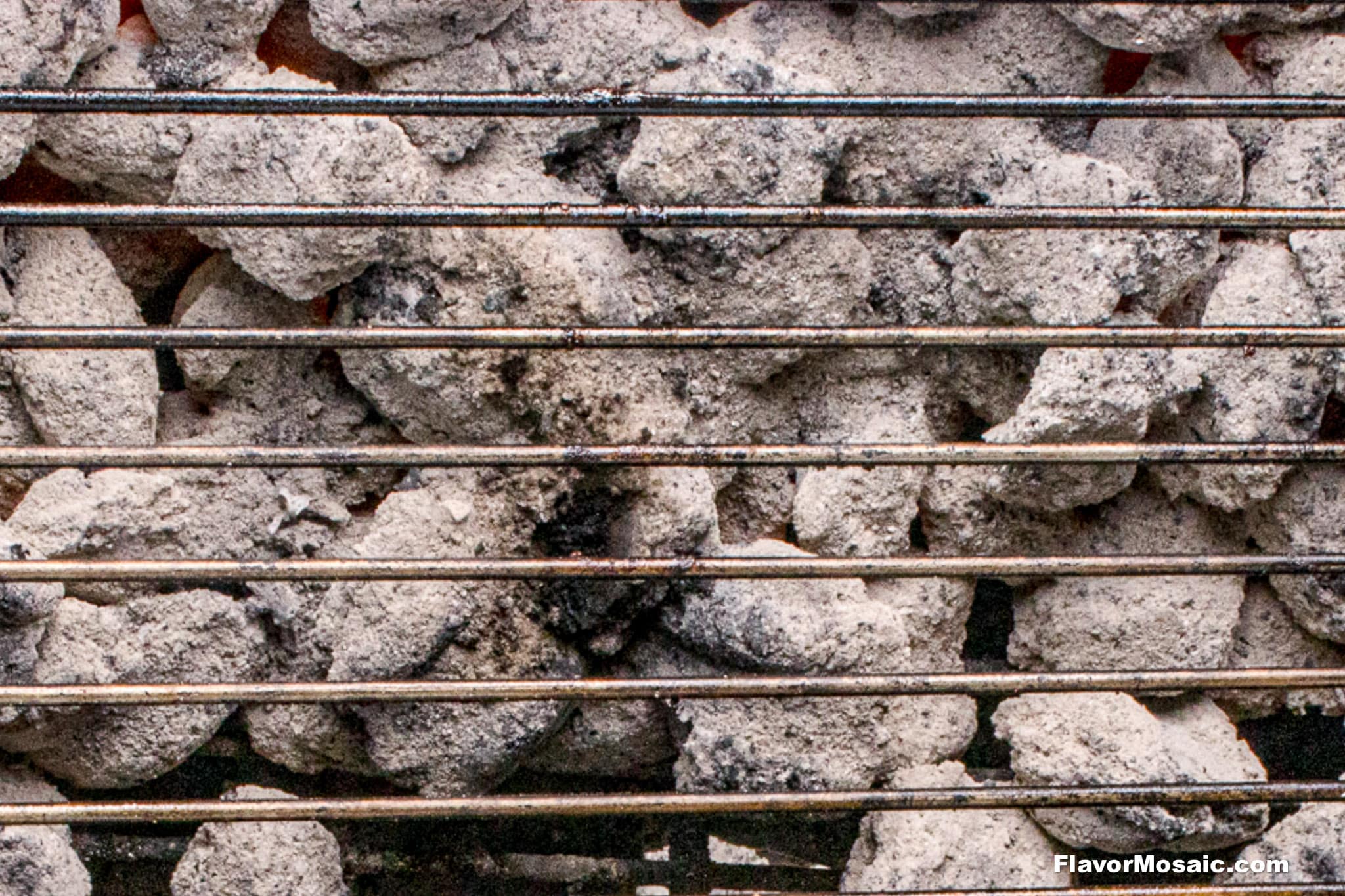 Close-up of a grill grate over ashy charcoal briquettes, ready for barbecuing. Perfect for grilling the best BBQ chicken legs, the metal bars run horizontally across the image above glowing coals.