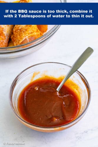 A small clear bowl with BBQ sauce and a spoon in it.