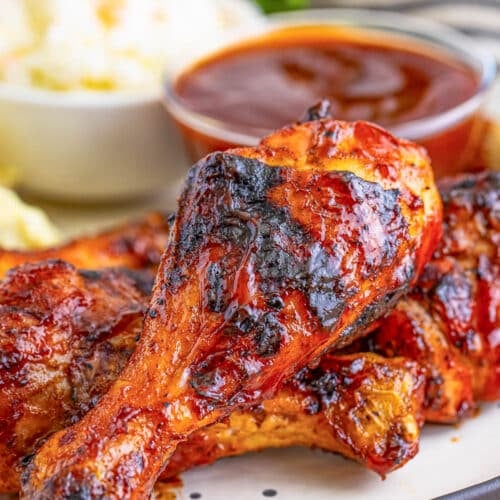 Grilled Chicken legs stacked on a plate with a small bowl of BBQ sauce