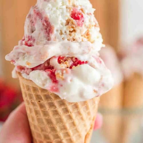 Someone holding a waffle cone with two scoops of Strawberry Cheesecake Ice Cream.