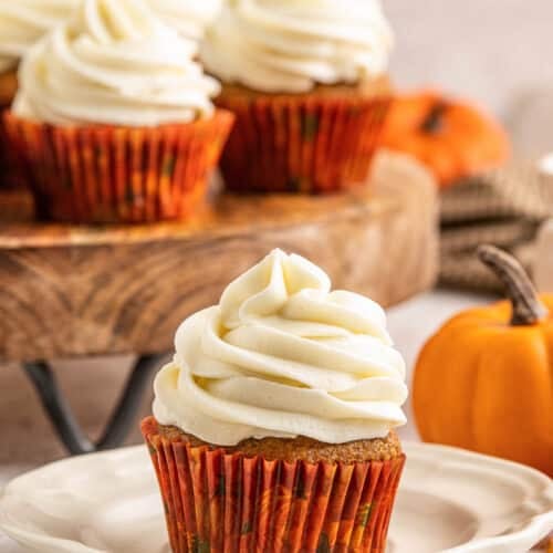 pumpkin cupcake on a white dish with more pumpkin cupcakes in the background.