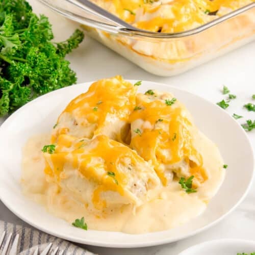 3 stuffed shells on a white plate with the casserole dish with more shells in the background.