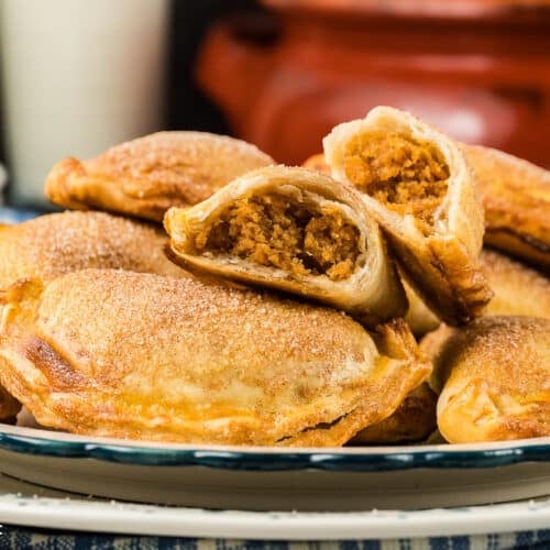 Cinnamon sugar coated sweet potato empanadas on a plate with one empanada cut in half to view the sweet potato filling.