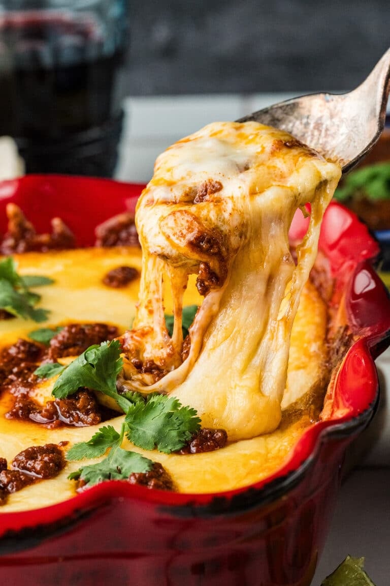 Cheese Pull with a spoon lifting the melted cheese from Queso Flameado with chorizo and cilantro from a bright red dish.