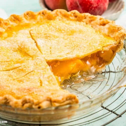 Peach pie in pie plate on cooling rack with two slices taken out of it.