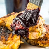 Brushing blueberry BBQ sauce on cooked chicken thighs with a jar of blueberry BBQ sauce in the background.