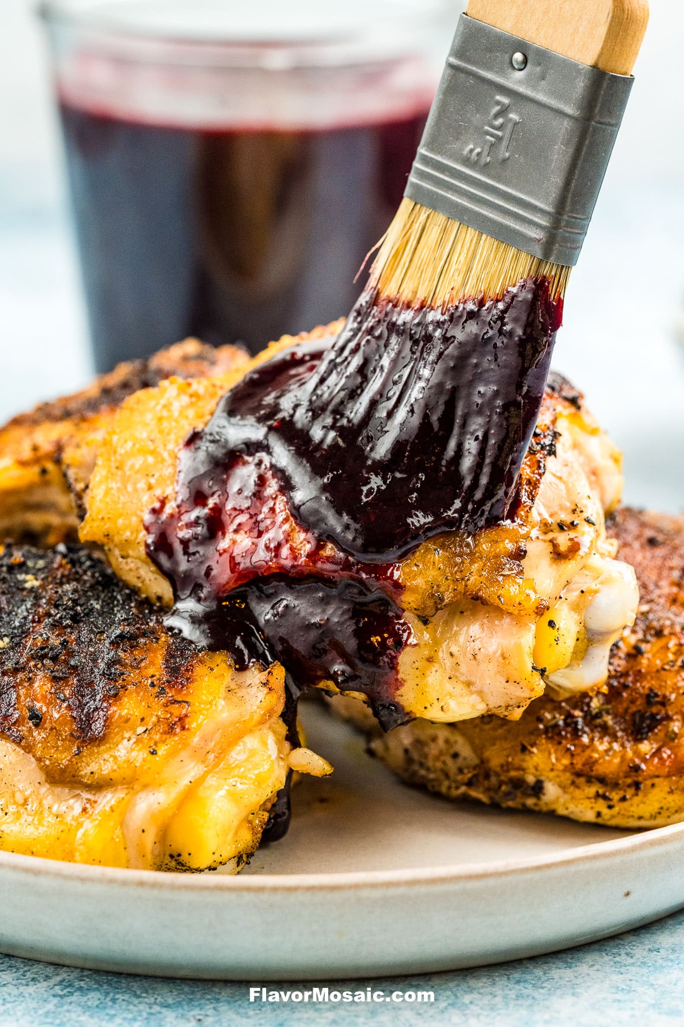 Brushing blueberry BBQ sauce on cooked chicken thighs with a jar of blueberry BBQ sauce in the background.