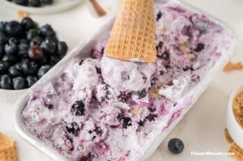 Cone on top of scoop of blueberry ice cream sitting on top of loaf pan with the rest of the blueberry pie ice cream.