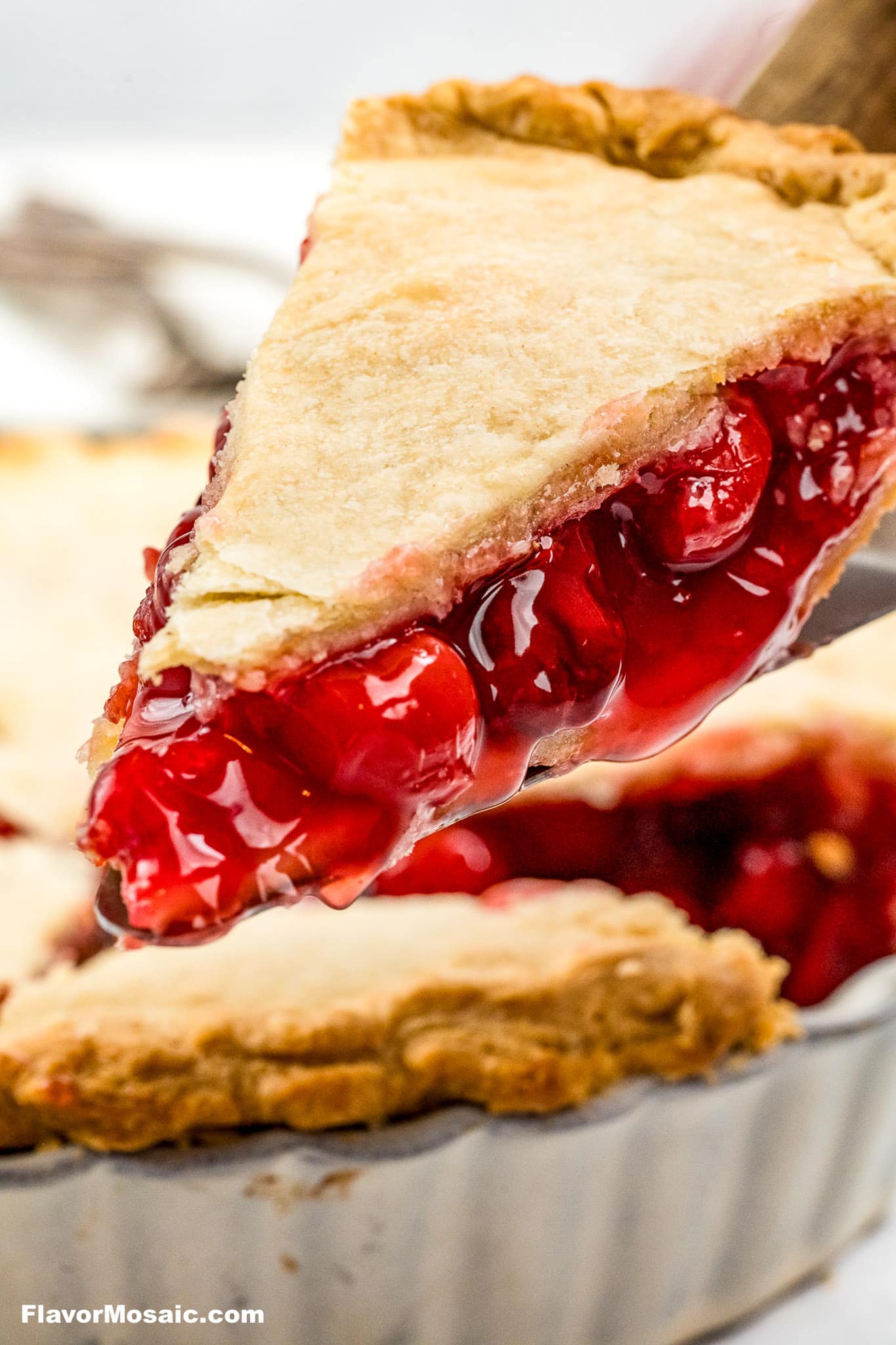 A slice of Cherry Almond Pie with a homemade pie crust on a spatula held above the rest of the pie.