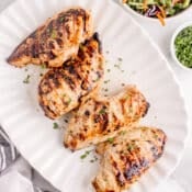 4 grilled chicken breasts on a white platter with a salad next to it.
