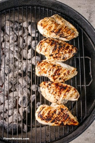 Grilled chicken breasts with grill marks moved to the cool side of the grill.