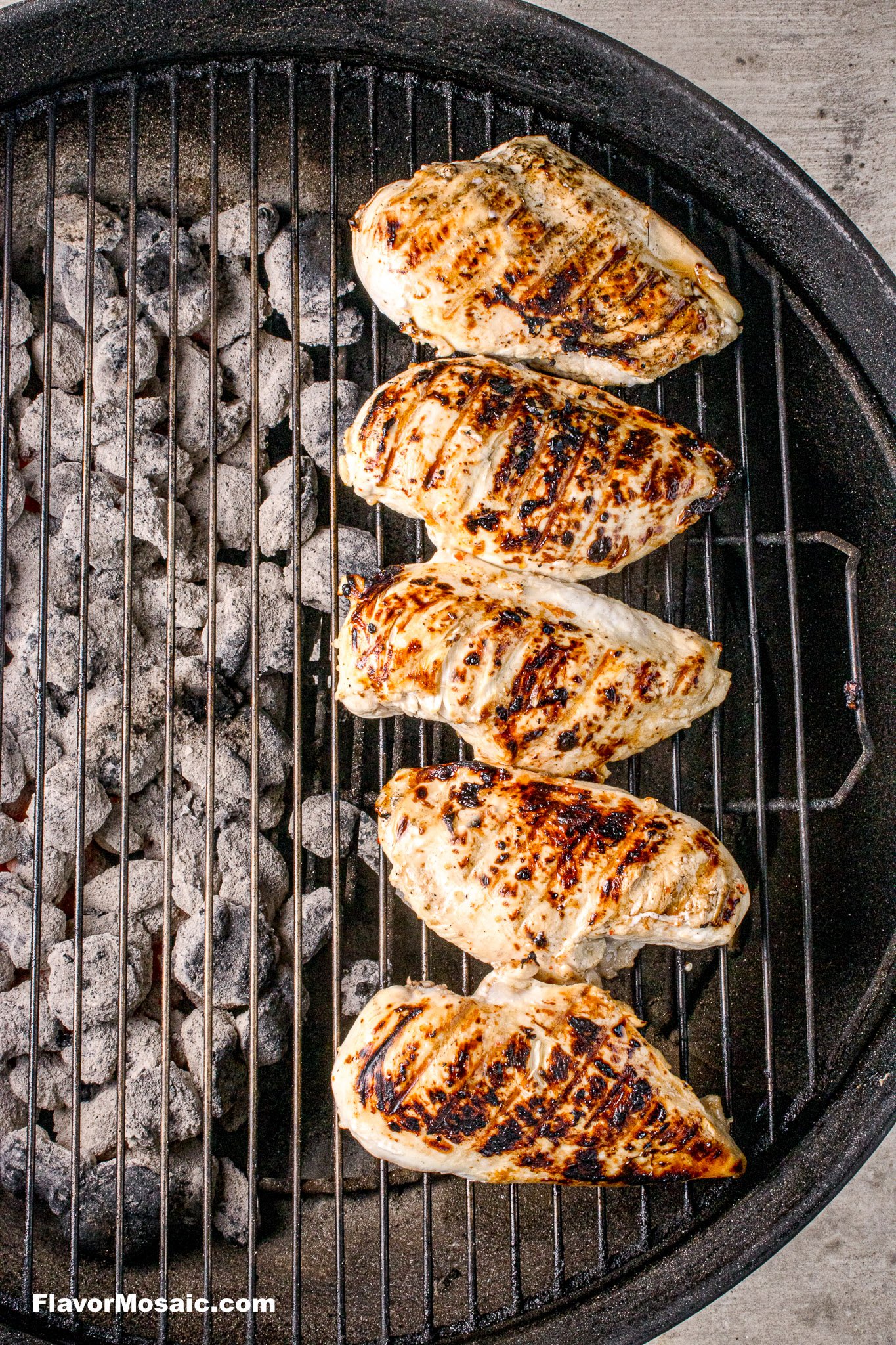 Grilled chicken breasts with grill marks moved to the cool side of the grill.