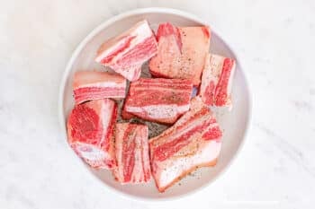 Beef Short Ribs on a white plate seasoned with salt and pepper.