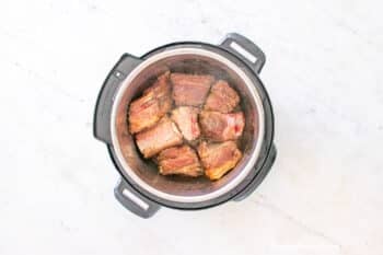 Beef short ribs inside an Instant Pot Pressure Cooking being sautéed before pressure cooking.