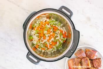 Chopped vegetables (carrots, celery, onion) inside an Instant Pot to be sautéed before pressure cooking short ribs.