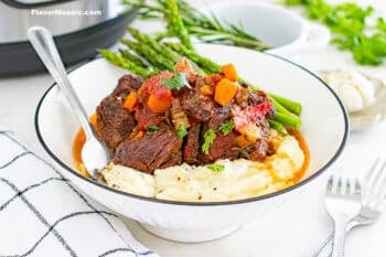 White bowl with Instant Pot Braised Beef Short Ribs over mashed potatoes and a side of asparagus.