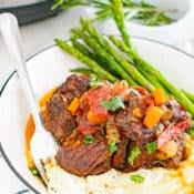3/4 view of a serving of Instant Pot Braised Beef Short Ribs over mashed potatoes with asparagus covered in a au jus sauce.