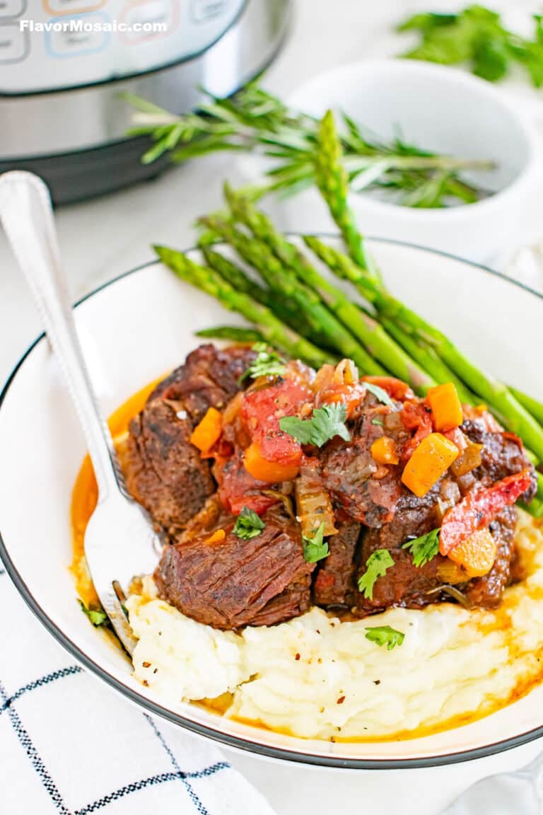 3/4 view of a serving of Instant Pot Braised Beef Short Ribs over mashed potatoes with asparagus covered in a au jus sauce.
